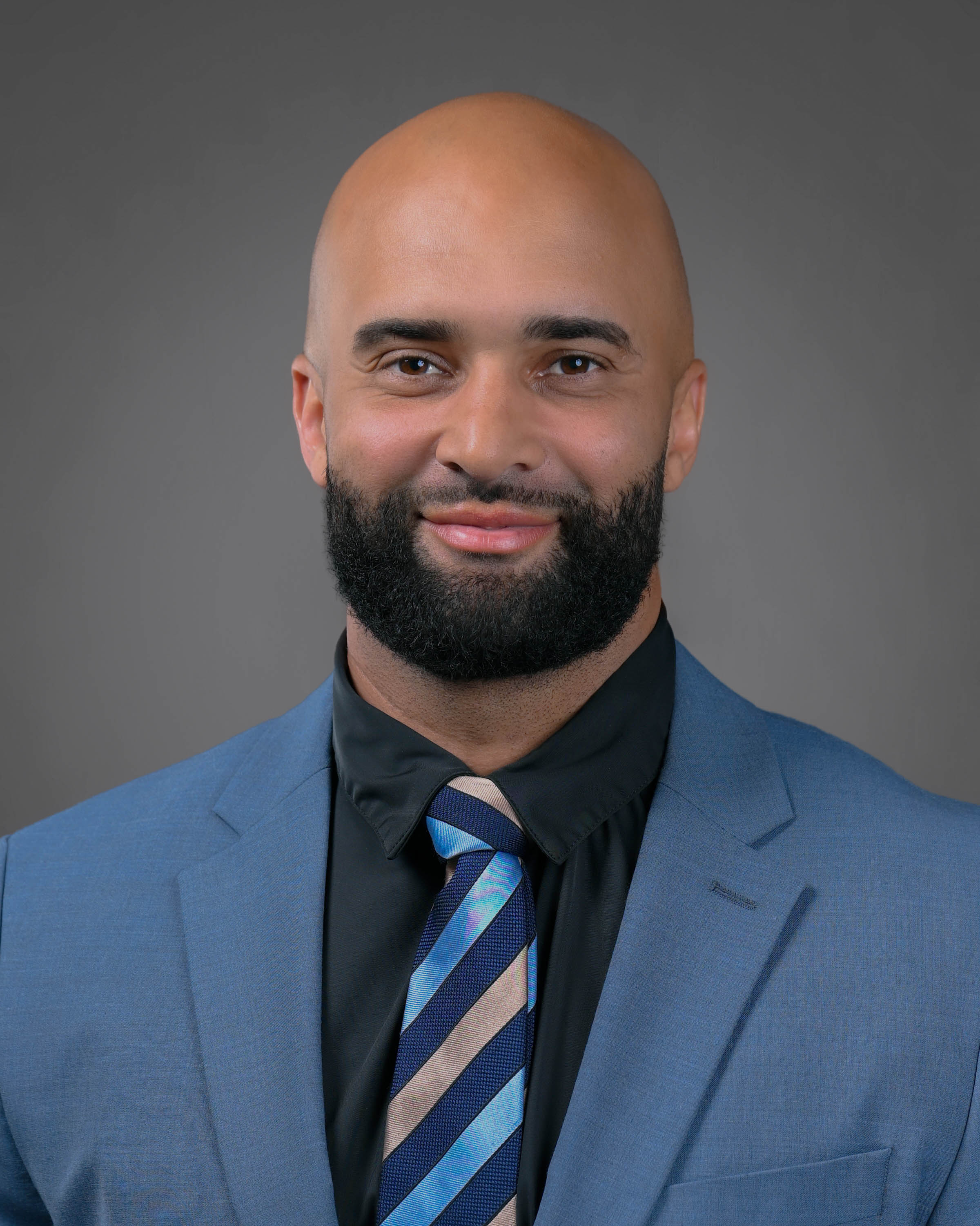 Man smiling with a beard and a clean shaven head in a blue suit